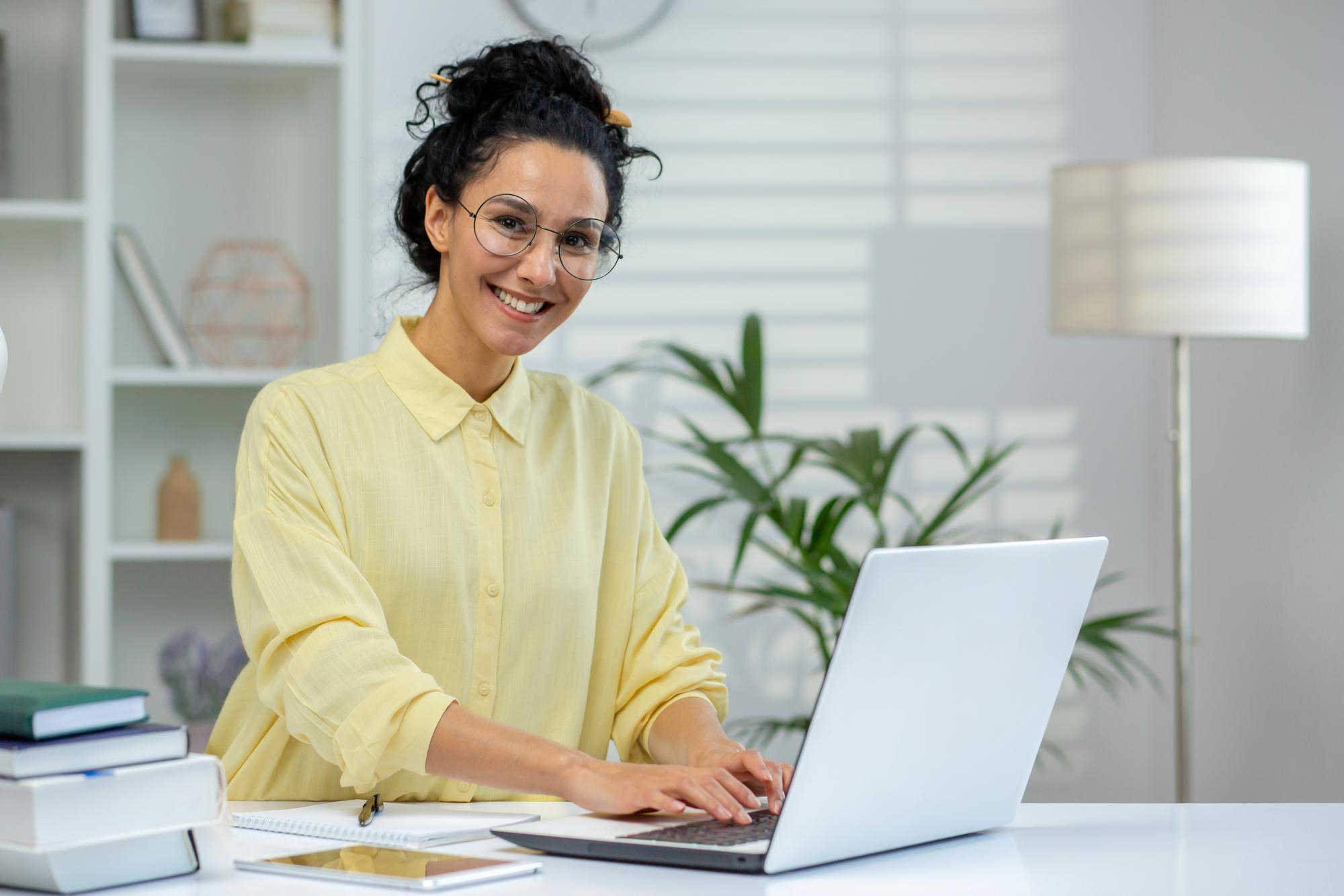 mulher jovem sorrindo com notebook na mesa utilizando o eLicitaProposta para o Portal e Compras Públicas